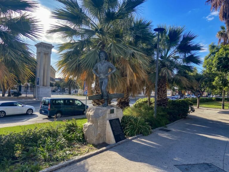 a statue of a man on a rock with palm trees in Malaga